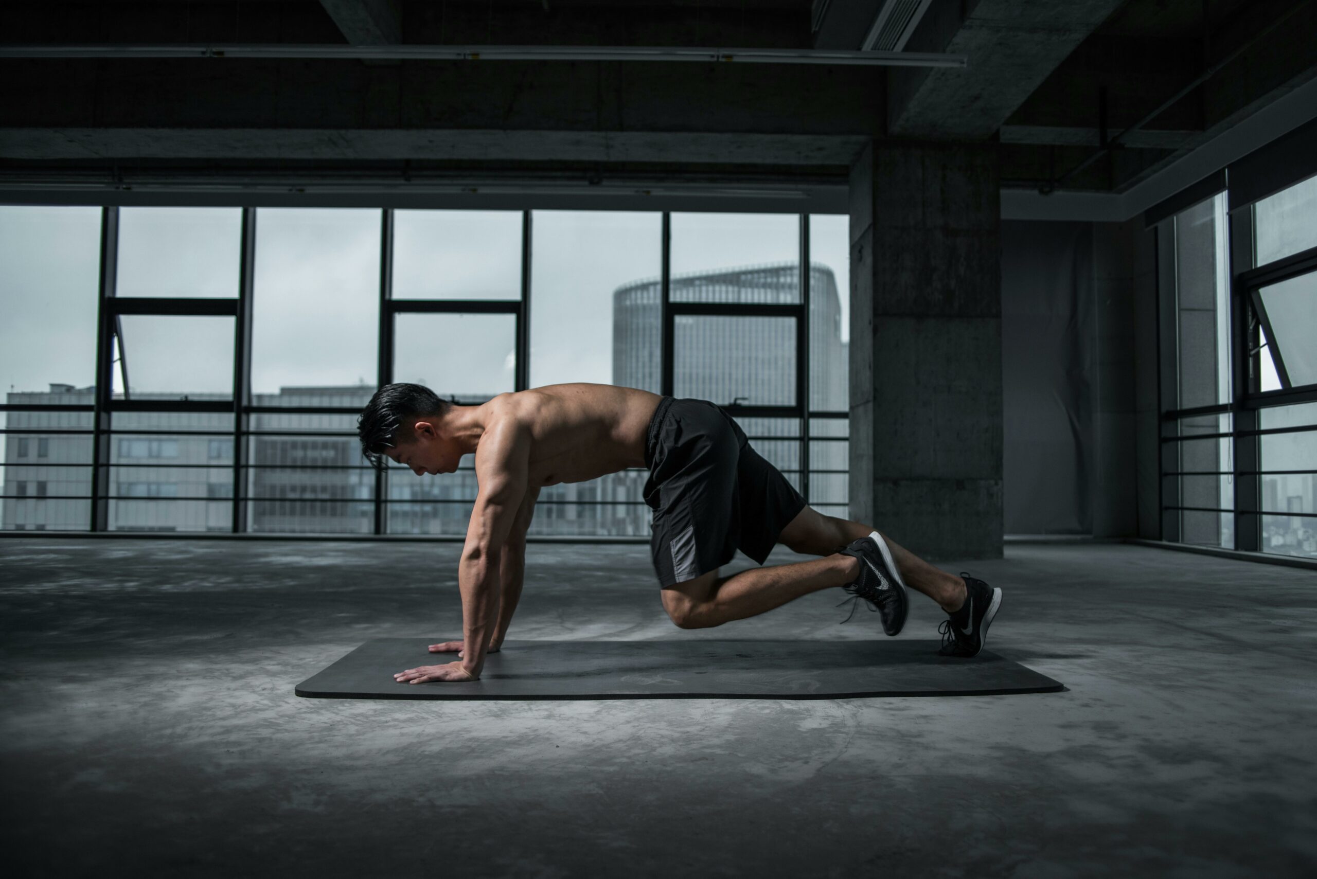 A man exercising on a mat in a room with many windows