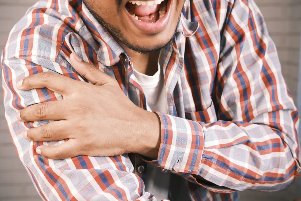 A man wearing a plaid shirt and grabbing his shoulder in pain.